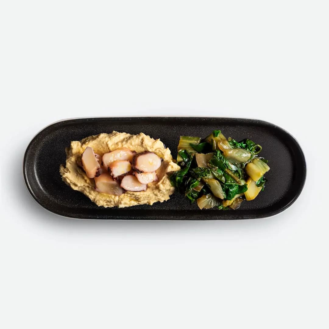 Octopus with chickpea purée and sautéed greens on a black oval plate