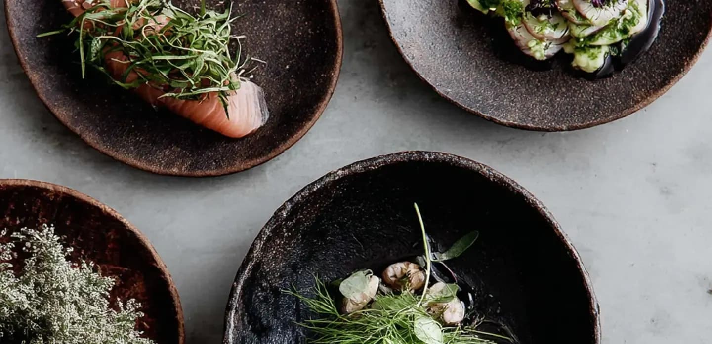 Rustic ceramic plates of fish and fresh herbs on a stone surface